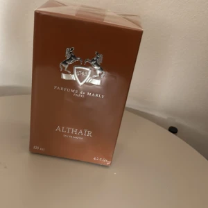 Parfums de Marly Althaïr 125ml - Lyxig parfym från Parfums de Marly, Althaïr, i en elegant brun kartong med silverdetaljer och logga. Eau de Parfum, 125 ml. Förpackningen är rektangulär och tillverkad av kartong, tillverkad i Frankrike.