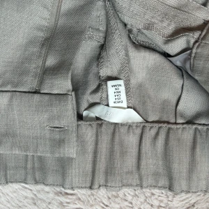 Beige kostymbyxor i linneblandning - Snygga beige kostymbyxor med rak passform och elastisk midja. Byxorna är tillverkade i en linneblandning som ger en avslappnad men ändå dressad känsla. Perfekta för dig som gillar stilrena och bekväma plagg.