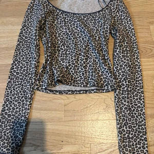 Leopardmönstrad långärmad topp - Säljer en snygg långärmad topp med leopardmönster i beige, svart och brunt. Toppen har rundad halsringning och är figurnära i modellen. Perfekt för dig som vill sticka ut med ett djurmönster och gillar trendiga plagg.