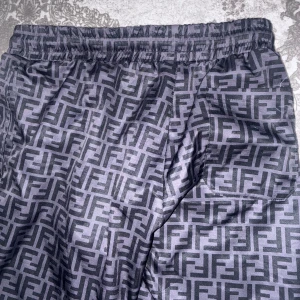 Svarta Fendi badshorts med FF-mönster - Snygga svarta badshorts från Fendi med ikoniskt FF-mönster över hela tyget. Shortsen har elastisk midja med snörning och innerbyxa i mesh. Perfekta för sommaren och poolhäng, riktigt lyxig vibe.