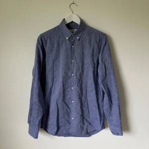 Blå skjorta från A Day's March M - Snygg blå skjorta från A Day's March i storlek M, tillverkad i tvåfaldig bomull. Skjortan har klassisk krage, knäppning framtill och långa ärmar med manschett. Slim fit-modell som sitter snyggt och stilrent. Artnr:C388