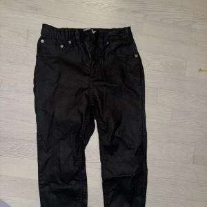 Svarta skinnbyxor  - Svarta skinnbyxor med smal passform och klassisk femficksdesign. Byxorna har dragkedja och knapp framtill samt bälteshällor i midjan. Snyggt stilrena och passar perfekt till sneakers eller boots.