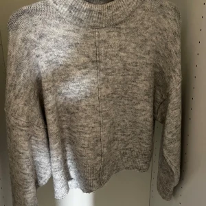 Grå stickadtröja Gina Tricot - Mysig gråmelerad stickad tröja från Gina Tricot. Tröjan har lite krage, lång ärm och en relaxed fit med ribbade muddar. 