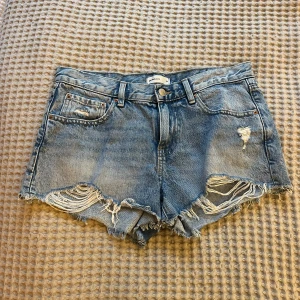 Blå jeansshorts - Snygga blå jeansshorts från Gina Tricot med fransiga kanter och slitna detaljer framtill. På mig sitter de som mid rise. Storlek 36. De är använde men är i bra skick. Säljer då jag har för många shorts.