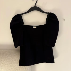 Svart topp med puffärm från H&M - Svart topp från H&M i storlek XS med trendiga puffärmar och fyrkantig ringning. Toppens material känns mjukt och stretchigt, perfekt för att lyfta vilken outfit som helst. Enkel men ändå snygg design som passar till många olika stilar.