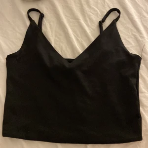 Svart croppad linnetopp från Amisu - Svart croppad linnetopp från Amisu med smala axelband och v-ringning. Enkel och stilren design som är lätt att matcha med olika outfits. Perfekt för dig som gillar minimalistisk stil och vill ha en topp som funkar till många looks.