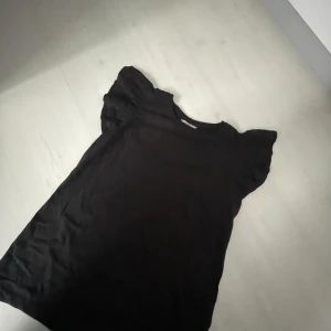 Svart topp med puffärm från TIKI - Supergullig svart topp som inte är använd så många gånger, är som en vanlig T-shirt men där är volanger istället för armar. 