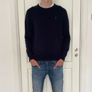 Mörkblå tröja från Ralph Lauren - Snygg mörkblå tröja från Ralph Lauren med klassisk rund hals och diskret broderad logga på bröstet. Tröjan är långärmad och har en stilren, enkel design som passar perfekt till jeans. Tillverkad i mjuk bomull för skön känsla.