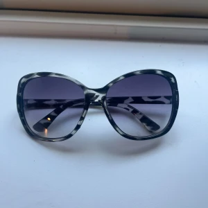 Svartvita mönstrade solglasögon - Stora solglasögon med svartvitt mönster och markerad båge i fjärilsform. Glasen är mörktonade och ger en cool vibe. 