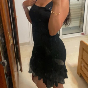 Svart kort volangklänning - Supersöt svart kort klänning med volangkant nertill och smala axelband. Sitter tajt och har en feminin siluett som framhäver formerna. Perfekt för dig som gillar en enkel men ändå snygg look. Materialet ser ut att vara stickat eller bomull.