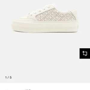 Vita sneakers från Tommy Hilfiger - Snygga vita sneakers från Tommy Hilfiger med beige monogrammönster på sidorna. Skorna har platt sula, rund tå och klassisk snörning. Ovandelen är i skinn och textil, skorna är i princip oanvända använts väldigt vaksamt 3-4 gånger i fint väder säljer pga ingen användning. Först till kvarn pris kan diskuteras vid snabb affär.