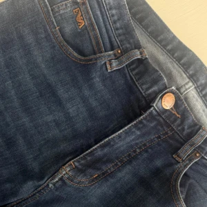 Emporio Armani blå jeans regular fit - Snygga blå jeans från Emporio Armani med klassisk femficksdesign, bruna sömmar och ikoniska EA-loggor i metall på fickorna. Regular fit-modell i mjukt bomullsjeansmaterial. Perfekta för dig som vill ha en stilren och tidlös look.