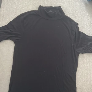 Svart polotröja från Gina Tricot - Svart polotröja från Gina Tricot i mjukt och stretchigt material. Klassisk modell med lång ärm och hög polokrage, perfekt att styla med jeans eller kjol. Enkel och stilren design som funkar till många olika looks.