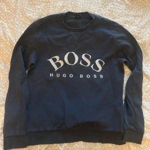 Mörkblå sweatshirt från Hugo Boss XS - Snygg mörkblå sweatshirt från Hugo Boss i storlek XS. Tröjan har broderad vit BOSS-logga framtill och klassisk rund halsringning. Tillverkad i mjuk bomull med långa ärmar och ribbade muddar för en clean och stilren look.