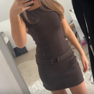Brun Zara klänning med bälte  - Helt ny, aldrig använd. Kort klänning med bälte som sitter fast. Bältet är endast på framsidan alltså går inte bakom klänningen. Storlek S men passar mig med Xs