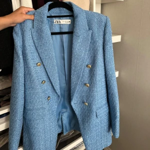 Blå kavaj med guldknappar från Zara - Snygg blå kavaj från Zara med strukturerat tyg och dubbla rader guldknappar framtill. Klassisk krage, långärmad och med fickor. Perfekt för dig som vill ha en stilren och trendig look.