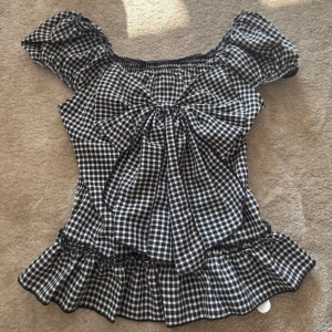 Rutig blus med rosett  - Supersöt svartvit rutig blus från Romwe med puffärmar, volangkant nertill och stor rosett framtill. Blusen har smockad rygg 