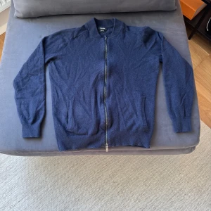 Marinblå ullkofta från Massimo Dutti - Snygg marinblå kofta i 100% extra fin ull från Massimo Dutti. Modellen har hel dragkedja framtill, ribbade muddar och två fickor. Perfekt för lager-på-lager och ger en clean look till din outfit. 