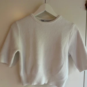 Vit stickad tröja från Zara - Superfin vit stickad tröja från Zara med ribbad rund hals och kortare ärmar. Tröjan har en mjuk och lite fluffig känsla, perfekt för dig som gillar en clean och enkel stil. Passar snyggt till både jeans och kjol.