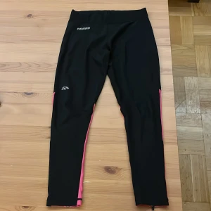 Svarta och rosa träningsleggings Karhu - Säljer ett par svarta och rosa träningsleggings från Karhu. De har dragkedjor vid bensluten, perforerade detaljer på baksidan av benen och är tillverkade i stretchigt material (88% polyester, 12% spandex). Perfekta för dig som gillar att träna med stil.