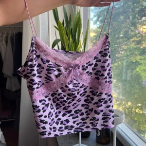 Lila leopardmönstrad linnetopp - Säljer en lila linnetopp med svart leopardmönster och tunna axelband. Toppen har spetsdetaljer och en liten rosett framtill, vilket ger en söt och trendig vibe. Perfekt för dig som gillar att sticka ut med färg och mönster.