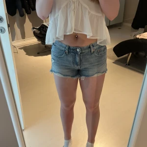 Blå jeansshorts från Gina Tricot - Snygga blå jeansshorts från Gina Tricot med råa kanter och klassisk femficksmodell. De är lågmidjade och har en avslappnad passform. Perfekta för sommardagar och festivalhäng. Materialet är jeans och färgen är ljusblå denim.