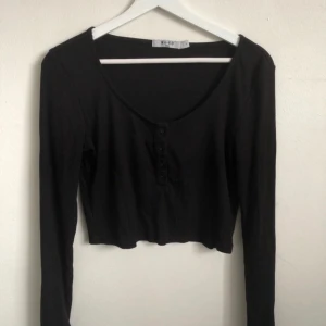 Svart croppad topp från NA-KD - Svart långärmad croppad topp från NA-KD med rund halsringning och knappar framtill. 