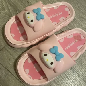 My Melody rosa sandaler med hjärtan - Supergulliga rosa sandaler med My Melody-motiv och blå rosett framtill. Sulan är dekorerad med vita hjärtan på rosa bakgrund och har en söt vågig kant. Perfekta för dig som älskar kawaii och vill ha något unikt på fötterna.