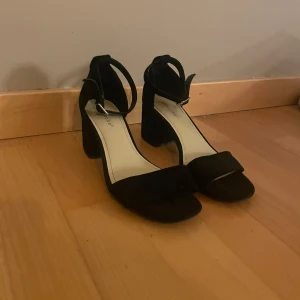 Svarta klackskor från Depeche - Svarta klackskor från Depeche med bred klack och öppen tå. Skorna har en enkel rem över tårna och justerbart spänne runt ankeln. Tillverkade i mocka💞jag har bara använt skorna en gång så de är lite slitna💗