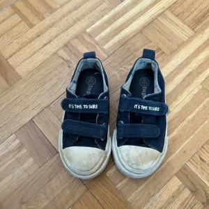 Mörkblå sneakers från Superfit strl 24 - Snygga mörkblå sneakers från Superfit med vita sulor och två kardborreband där det står 'IT'S TIME TO SURF'. Skorna har rund tå och är tillverkade i textil med mönstrat innerfoder. Perfekta för en avslappnad och cool stil.