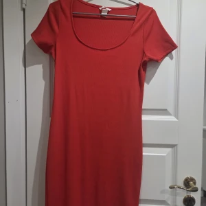 Röd ribbad kortklänning med rund hals - Enkel och snygg röd kortklänning med ribbad struktur och rund, djup ringning. Klänningen har korta ärmar och en figurnära passform som passar perfekt till sommaren. Stilren och lätt att matcha med accessoarer.