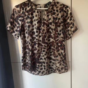  blus från Stockh LM - Säljer en snygg blus från Stockh LM i storlek 36 med leopardmönster i beige, brunt och svart. Blusen har korta ärmar och en liten öppning framtill vid halsen. Perfekt för dig som vill sticka ut med ett coolt mönster.