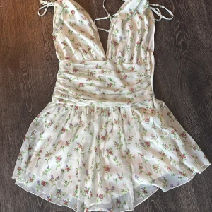 Blommig kortklänning från NA-KD - Supersöt kortklänning från NA-KD. Djup v-ringning, tunna axelband med knyt. Använd ett fåtal gånger 