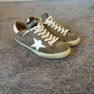Beige mocka sneakers från Golden Goose - Snygga beige sneakers från Golden Goose med vit stjärndetalj på sidan och vit hälkappa. Skorna har snörning och är gjorda i mocka med en klassisk låg profil. Perfekta för dig som gillar en avslappnad men trendig stil.