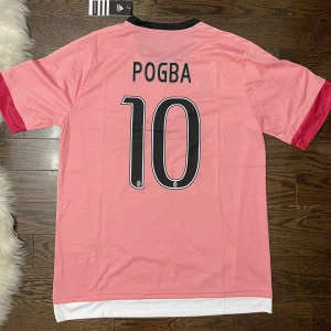 Juventus Pogba rosa fotbollströja - Rosa fotbollströja från Juventus med Pogba och nummer 10 på ryggen i storlek S och M . Tröjan har svarta detaljer, korta ärmar med röda muddar och Champions League-märke på ärmen. Helt ny och oanvänd, så finns inge defekter, hör av er