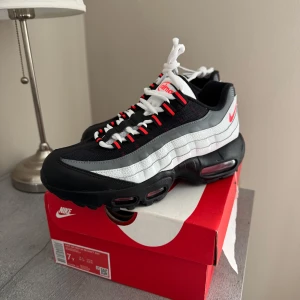 Nya Nike Air Max 95 svart/vit/röd - Nike Air Max 95 sneakers i svart, vitt och grått med röda detaljer. Skorna har en chunky sula med synliga Air-enheter, mesh och syntetmaterial i ovandelen samt klassisk snörning. Perfekt för dig som gillar streetwear och sportig stil. Helt nya skolåda finns. 