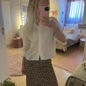 Vit broderad blus  - Supersöt vit blus med broderade blommor och knappar framtill. Blusen har lång ärm, krage med vågig kant och är gjord i tunn bomull. Snygg att styla med både kjol och jeans.