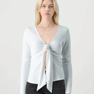 Vit långärmad knytblus - Snygg vit långärmad blus med djup v-ringning och knyt framtill. Toppens material är mjukt och lätt, perfekt för att skapa en trendig look. Passar till både jeans och kjol för en cool stil. Aldrig använd 