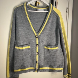 Grå kofta med gula ränder från Zara - Grå stickad kofta från Zara med gula ränder längs kanter, ärmar och fickor. Knappt använd och i jättefint skick och i storlek s