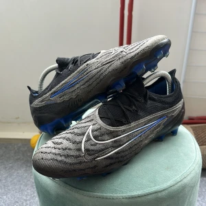Nike Phantom GX Elite FG Shadow - ⚽️ Nike fotbollsskor Säljer mina skor då de inte passar längre. De är ganska använda men fortfarande i bra skick för spel! Nypris var ca 3200 kr.  💸 Mitt pris: 700 kr  Perfekt för någon som vill ha ett par kvalitetsdobbar utan att betala fullpris! Pris går att diskutera privat! 
