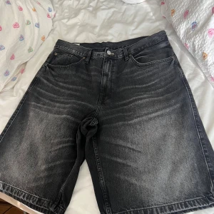 Svarta jeansshorts från Zara - Säljer ett par svarta jeansshorts från Zara med klassisk femficksdesign och knappstängning. Modellen är loose fit med raka ben och midwaist. Materialet är robust denim och färgen har en snygg tvättad look som ger lite edge.