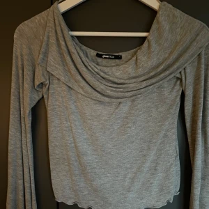 Grå offshoulder topp Gina Tricot - Jag säljer en ljusgrå offshoulder topp från Gina Tricot. Toppen har långa ärmar och en vågig kant nertill.
