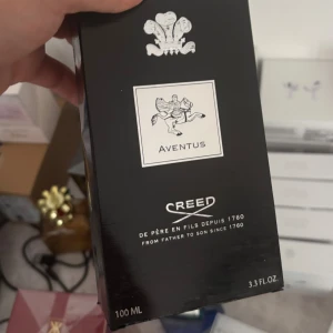 Creed Aventus 100ml parfym - Lyxig parfym Creed Aventus i svart och silver kartong, 100 ml. Känd för sin ikoniska doft och exklusiva känsla. Förpackningen har en elegant design med silverdetaljer och klassisk logotyp. Perfekt för dig som vill sticka ut med en tidlös och kraftfull doft.