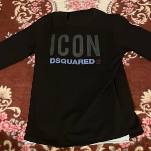 Svart långärmad tröja Dsquared2 ICON - Svart långärmad tröja från Dsquared2 med stor 'ICON' printad framtill i svart och blått. Tröjan har en klassisk passform och är perfekt för dig som gillar streetwear och vill sticka ut med en snygg logga.