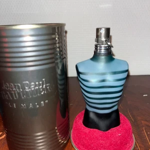 Jean Paul Gaultier Le Male parfym - Ikonisk parfym i blå och svart flaska formad som en manlig torso med horisontella ränder. Kommer med original metallburk. Flaskan har en modern och stilren design som sticker ut på hyllan. OBS hälften kvar av 75 ml