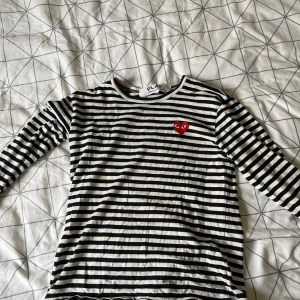 Randig långärmad tröja Comme des Garçons - Säljer en svartvit randig långärmad tröja från Comme des Garçons Play. Tröjan har ett ikoniskt rött hjärta med ögon broderat på bröstet och är tillverkad i mjuk bomull. Perfekt för dig som gillar stilrena och coola plagg.