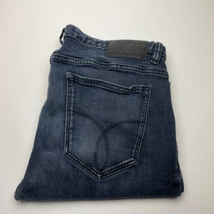 Calvin Klein jeans  - Snygga mörkblå jeans från Calvin Klein Jeans med klassisk femficksdesign och diskret logga på bakfickan. Jeansen har raka ben och är tillverkade i mjukt denimtyg som sitter skönt hela dagen. Perfekta för en stilren och avslappnad look.