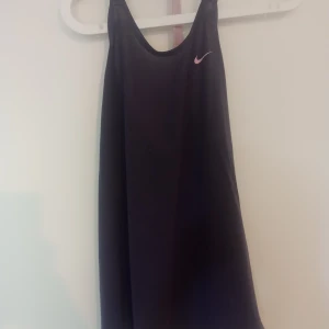 Lila Nike Dri-Fit linnetopp S - Sportig lila linnetopp från Nike med Dri-Fit-teknologi. Toppen har racerback med ett brett band där det står 'NIKE' och en liten vit swoosh på framsidan. Perfekt för träning och aktiva dagar, tillverkad i mjukt syntetmaterial som andas.