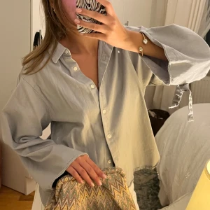 Ljusgrå oversized jeansskjorta - Säljer en ljusgrå oversized jeansskjorta med knappar framtill och breda ärmar med snygg knyt-detalj vid handlederna. 