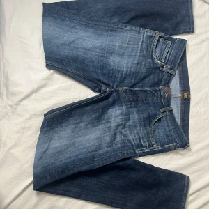 Blå Lee jeans i ekologisk bomull - Säljer ett par klassiska blå jeans från Lee i ekologisk bomull. Jeansen har en snygg tvätt med ljusare partier, raka ben och femficksmodell. Gula kontrastsömmar och Lee-logga på knappen och etiketten. Perfekta för en avslappnad och stilren look. Str 42 W 44 L